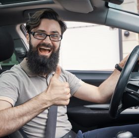 Man driver happy smiling showing thumbs up driving sport car with city buildings in background. Handsome young man excited about his new vehicle. Positive face expression